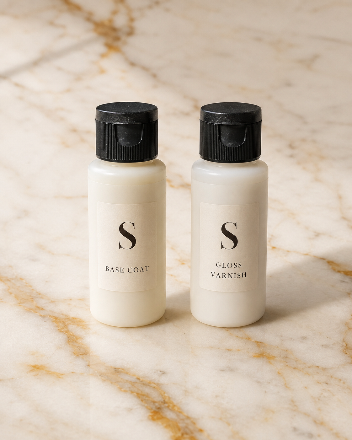 Two small white bottles with black caps labeled 'S BASE COAT' and 'S GLOSS VARNISH' standing side by side on a beige marble surface with gold veining.