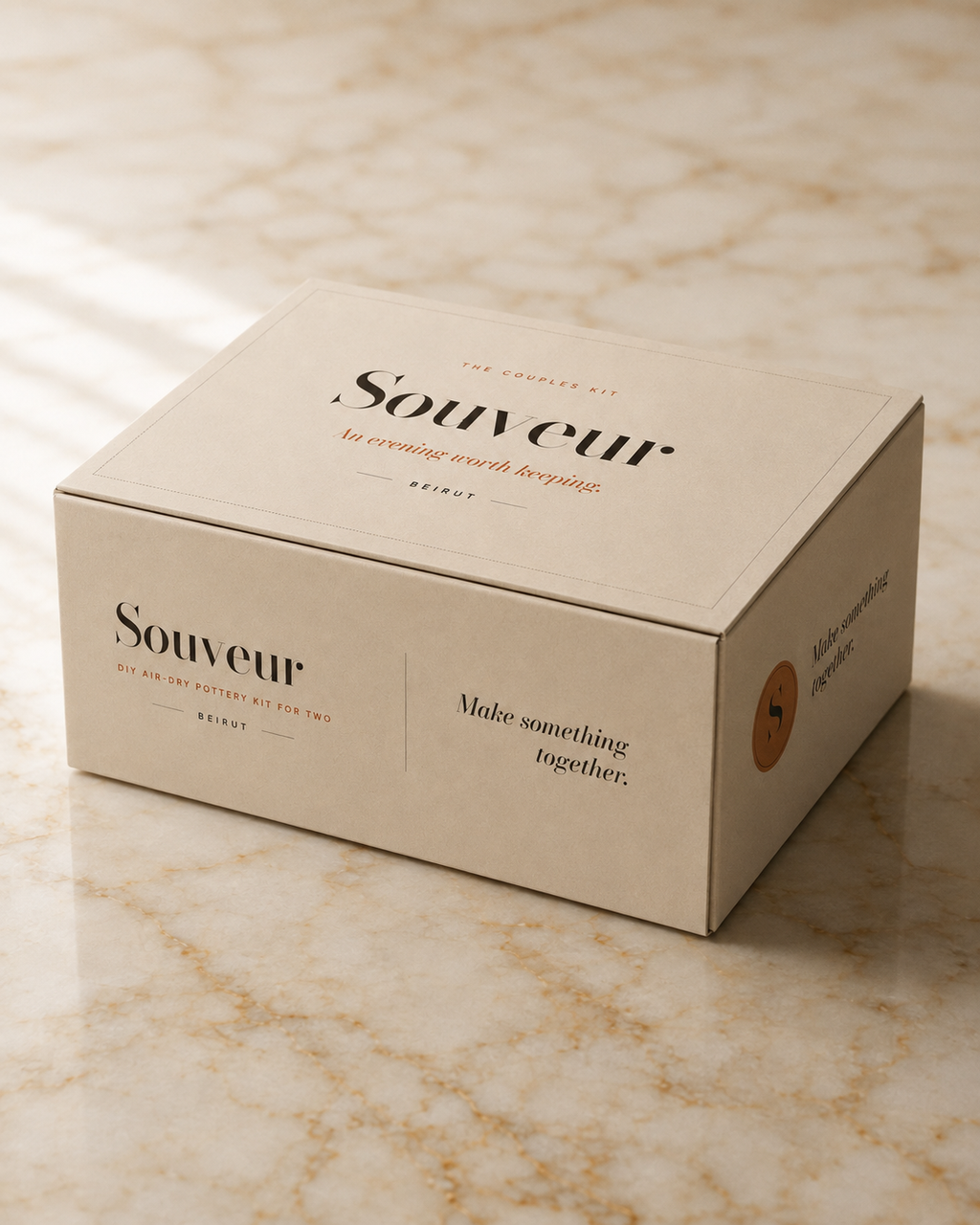 A beige Souveur gift box with elegant black and orange typography, resting on a polished beige marble surface.
